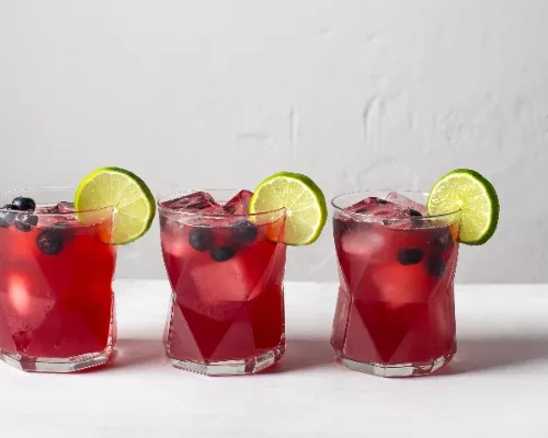 Trois verres de cocktail de bière aux bleuets garnis de bleuets et de lime