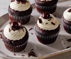 Cinq petits gâteaux Forêt Noire avec glaçage chantilly, garnis de cerises et de copeaux de chocolat sur un plateau.