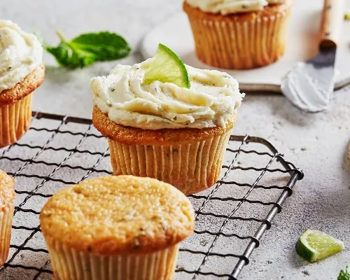 Cupcakes style Mojito sur une grille de refroidissement, certains recouverts d'un glaçage à l'hermine et garnis de citron vert.
